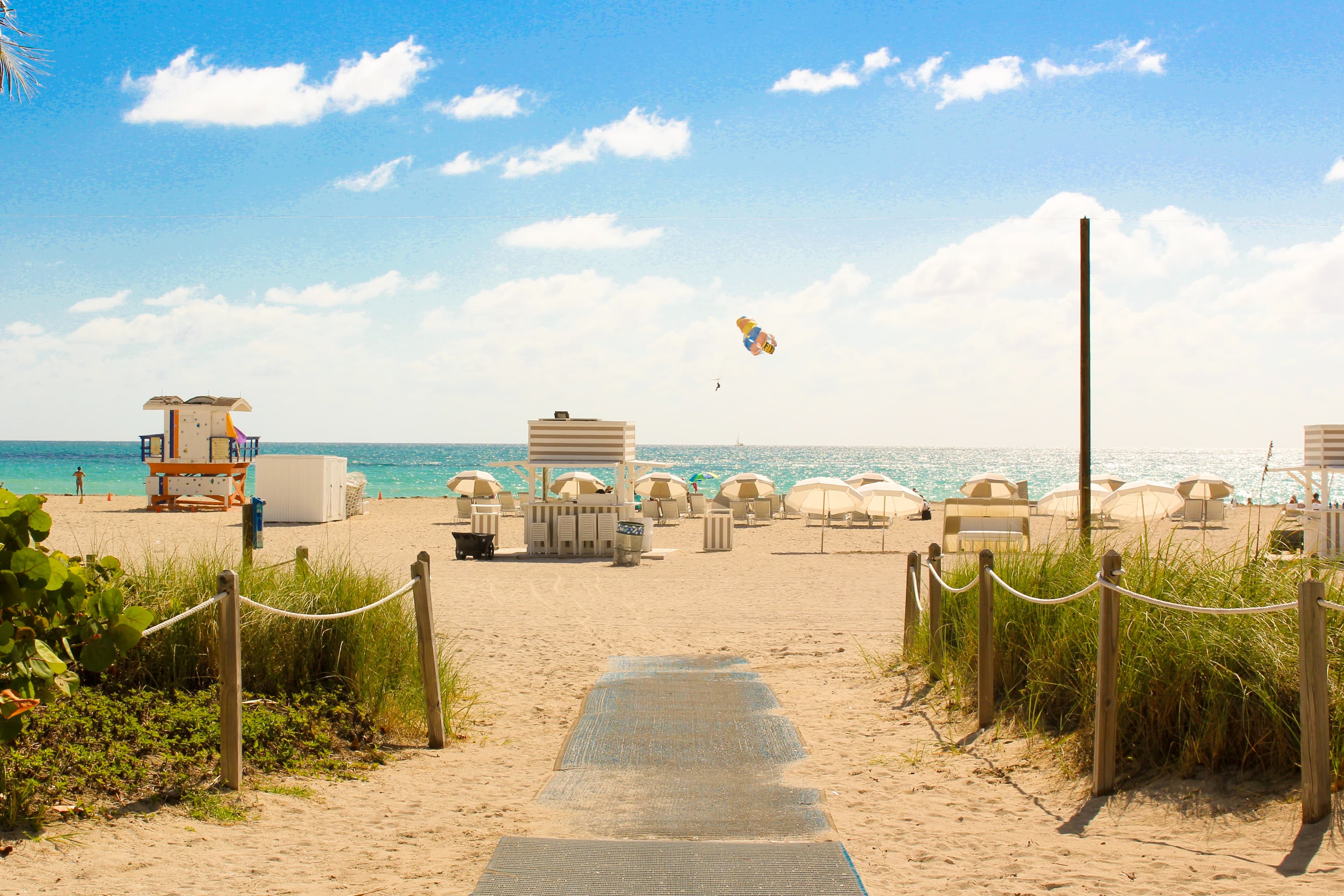 This is a photo of a path to a Florida beach, There are chairs and a life guard stand set up on the sand and tall green grass lining the path.